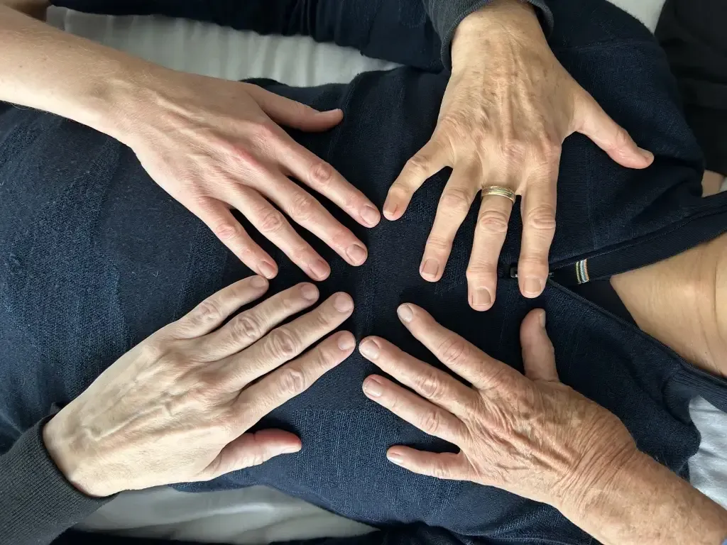 Frederick, MD CranioSacral Therapist Lori Leitzel Rice, haired pulled back and in a black tank top, stands next to a sculpture of two hands coming together