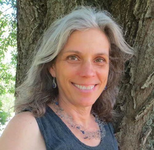 Frederick, MD CranioSacral Therapist Lori Leitzel Rice, haired pulled back and in a black tank top, stands next to a sculpture of two hands coming together
