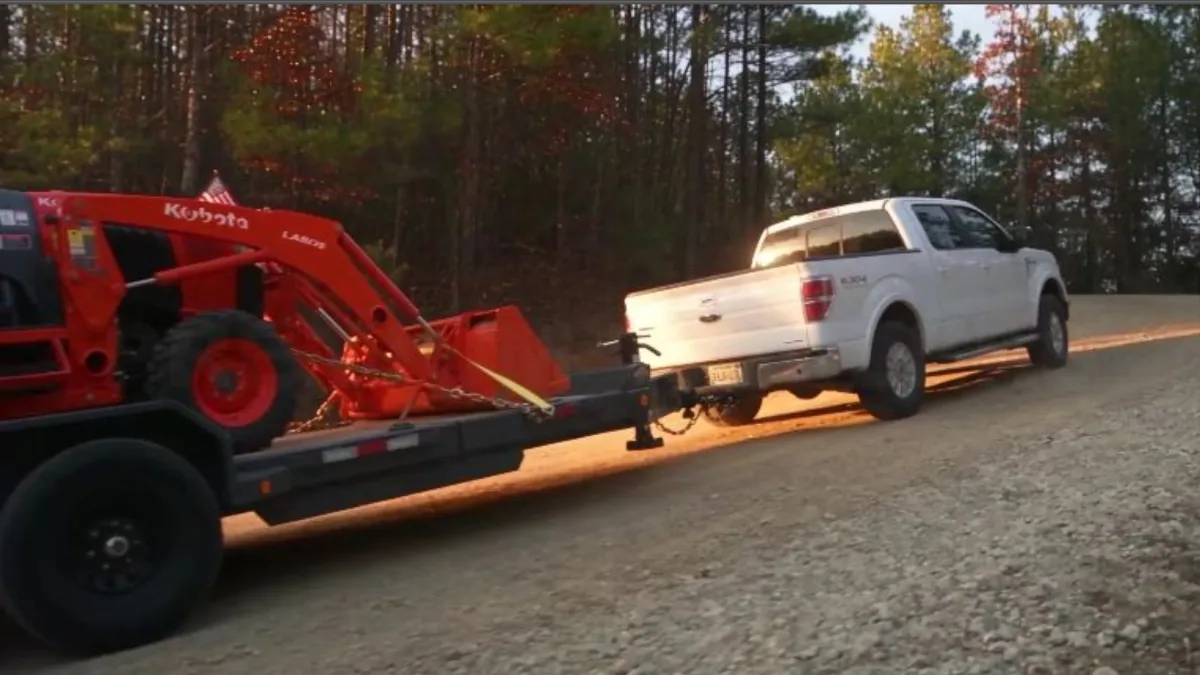 Iron Bull tilt-deck trailer loaded with bundled materials being towed by a pickup truck