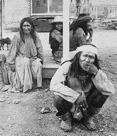 Chiricahua Apache individuals seated and standing near a building, depicting their resilience and cultural heritage in the context of historical displacement and community rebuilding efforts.