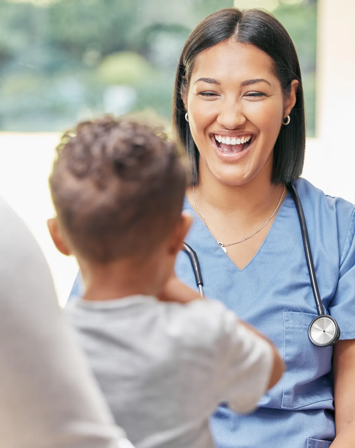 Nurse in a blue uniform smiling gleefully at a baby patient.