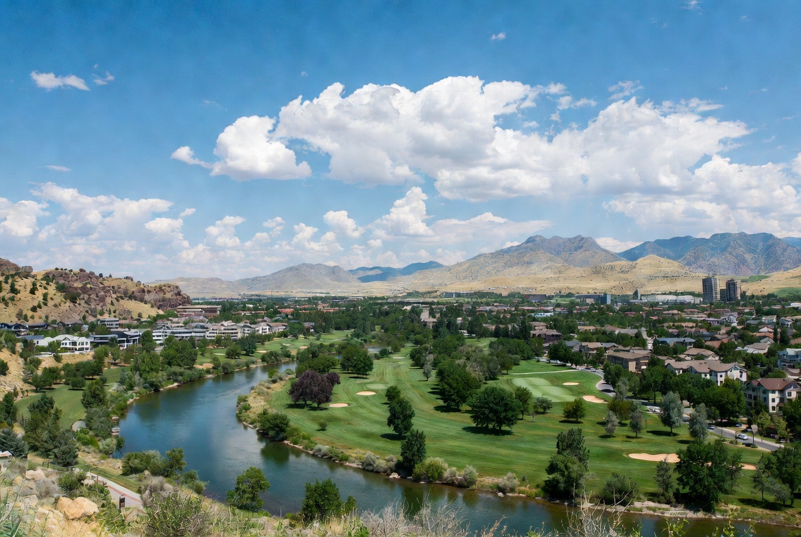 Aerial view of Eagle, Idaho showing the Boise River winding through a lush green golf course, with the foothills and surrounding skyline in the distance under a bright blue sky with scattered clouds.