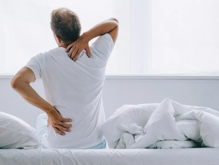 Man sitting on edge of bed with back pain