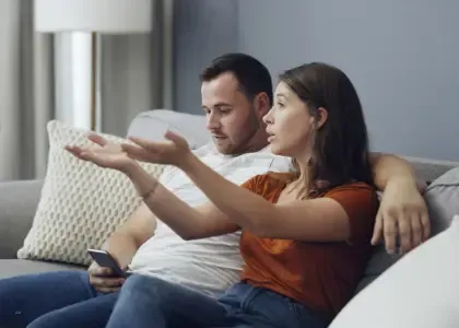 Photo of a couple sitting on a couch during a conversation, one partner speaking while the other appears distracted, representing emotional disconnection, misalignment, and early relationship tension before clarity