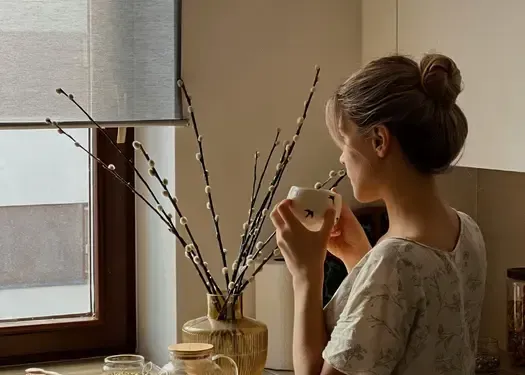 Woman looking out a window while holding a warm drink and reflecting on personal growth, self-discovery, and relationship dynamics.