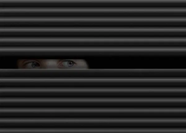Eyes peering through window blinds, representing suspicion and uncertainty about possible betrayal in a relationship