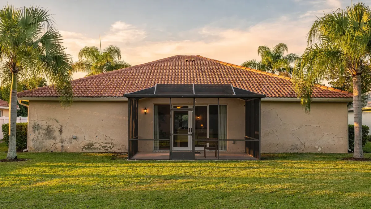 Rear view of a Fort Pierce stucco ranch home with screened lanai and palms