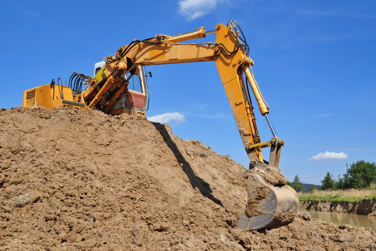 Excavator performing site work beside a mound of soil