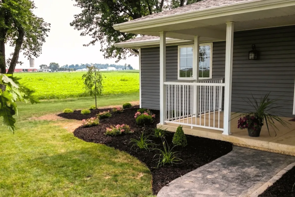 Newly installed residential landscape bed with mulch, plants, and a front walkway