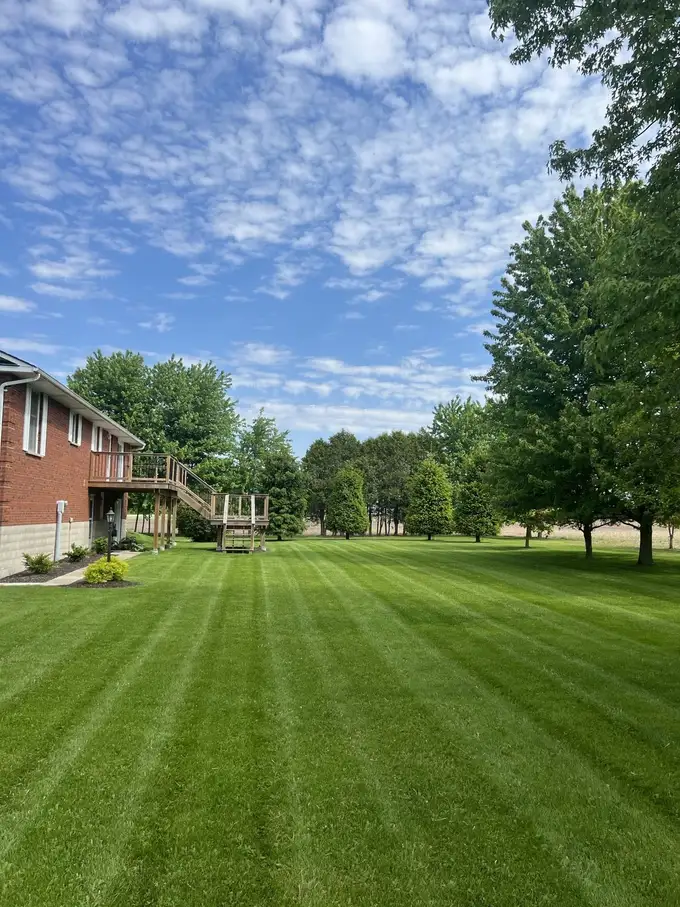 Striped lawn on a large country property beside a brick house with mature trees