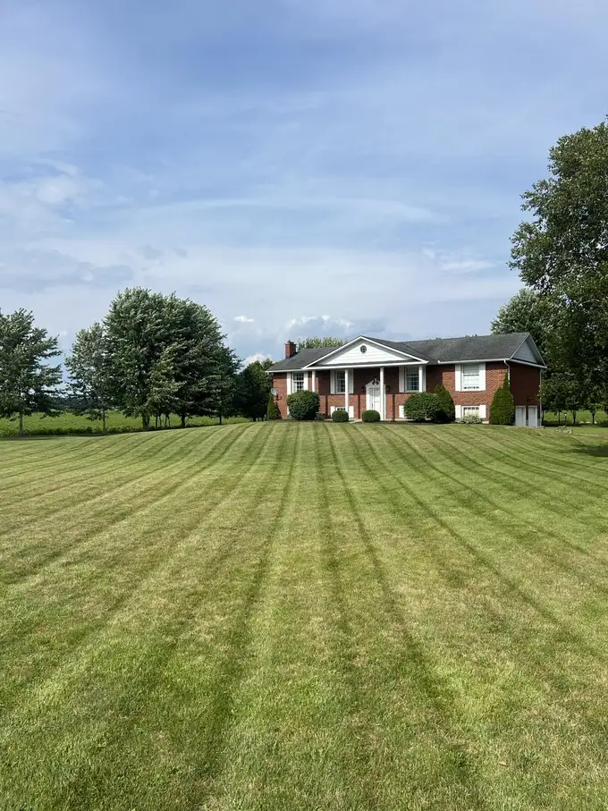 Long striped front lawn leading to a brick estate home in the countryside