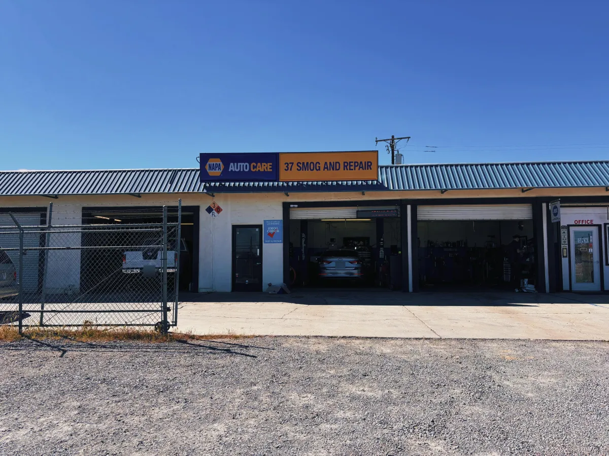 Exterior view of 37 Smog and Repair shop showing three open service bays, a vehicle inside, and Napa Auto Care signage under a clear blue sk