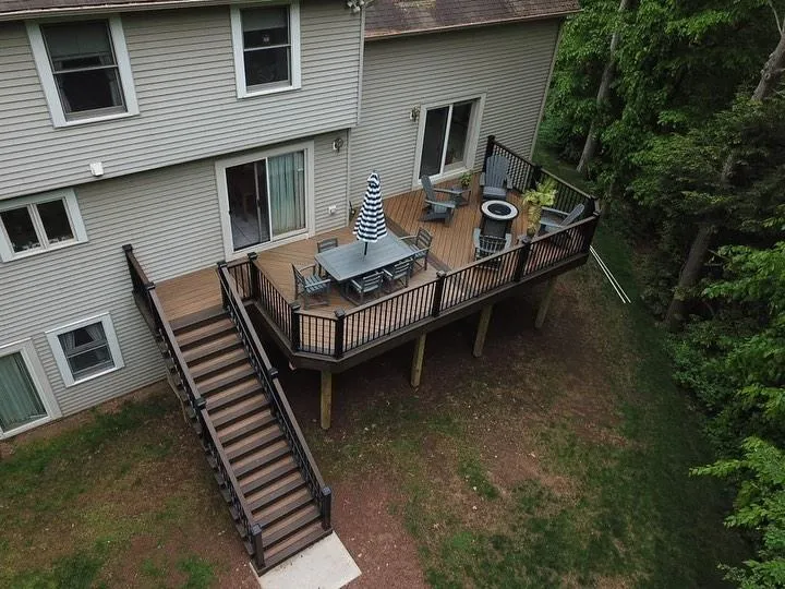 Multi-level brown composite deck with black railings, a dining set and an umbrella in a wooded yard | Prime Decks Delaware, serving New Castle County, DE