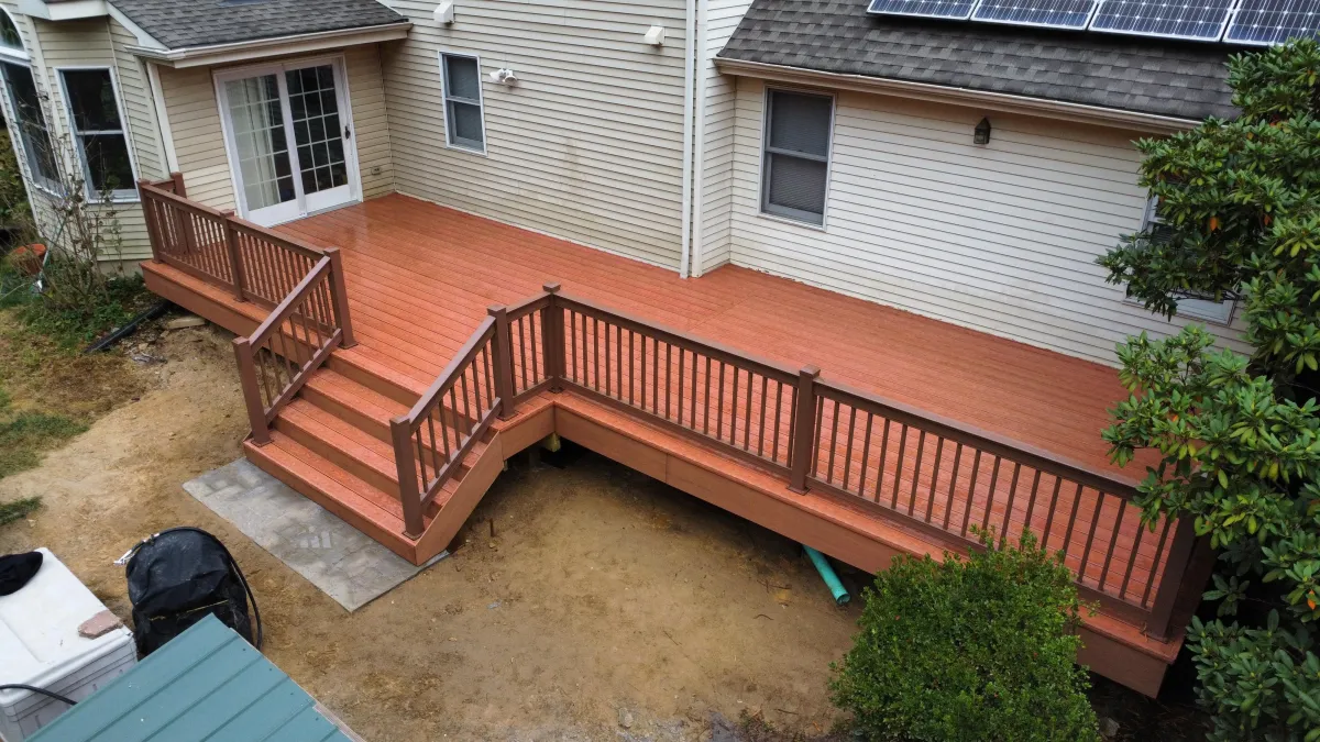 Red-brown wood-tone deck with matching railings and wide steps on a tan home | Prime Decks Delaware, serving Newark, DE