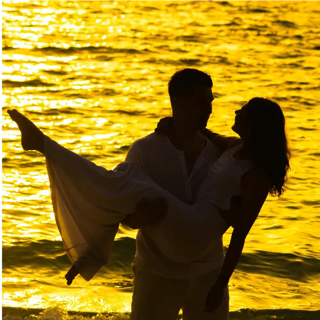 beach scene of man and woman looking at each other as he carries her