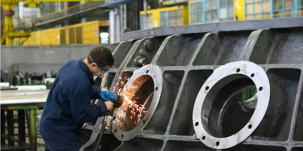 Factory worker operating equipment on a large metal assembly, representing high-stress and shared industrial workspaces where Calm Work Solutions kits support focus and calm.