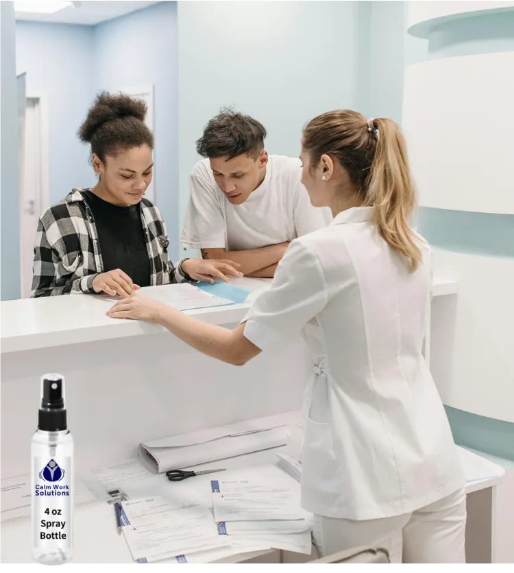 Workplace scene showing an employee handing papers to two coworkers at a reception desk, with a Calm Work Solutions spray bottle nearby to illustrate on-the-job use.