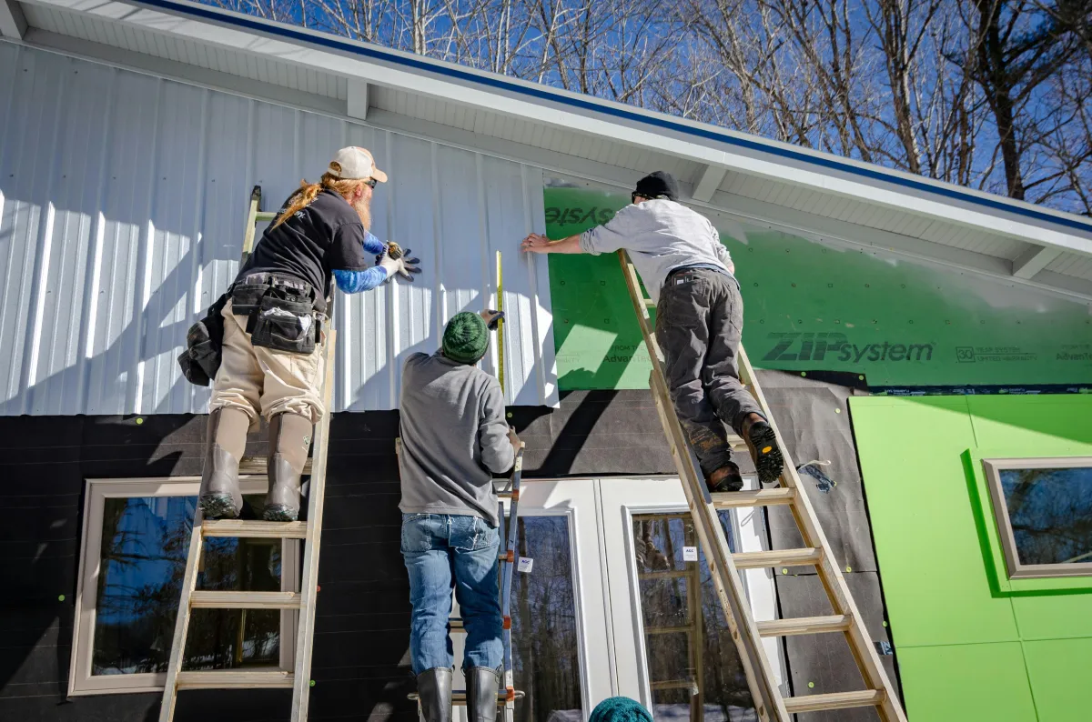 three siding installers on ladders working together 