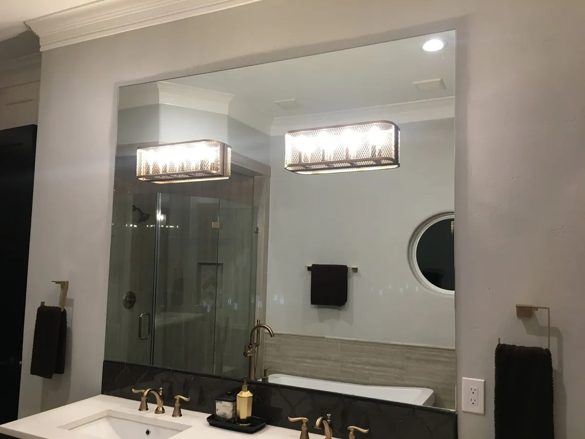 Custom frameless mirror over a vanity with sconces