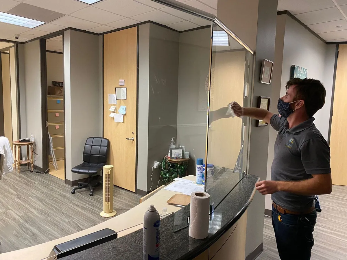 Installer fitting a glass sneeze guard at a reception desk