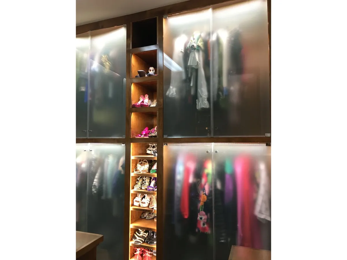 Lit closet with glass shelving and frosted glass doors
