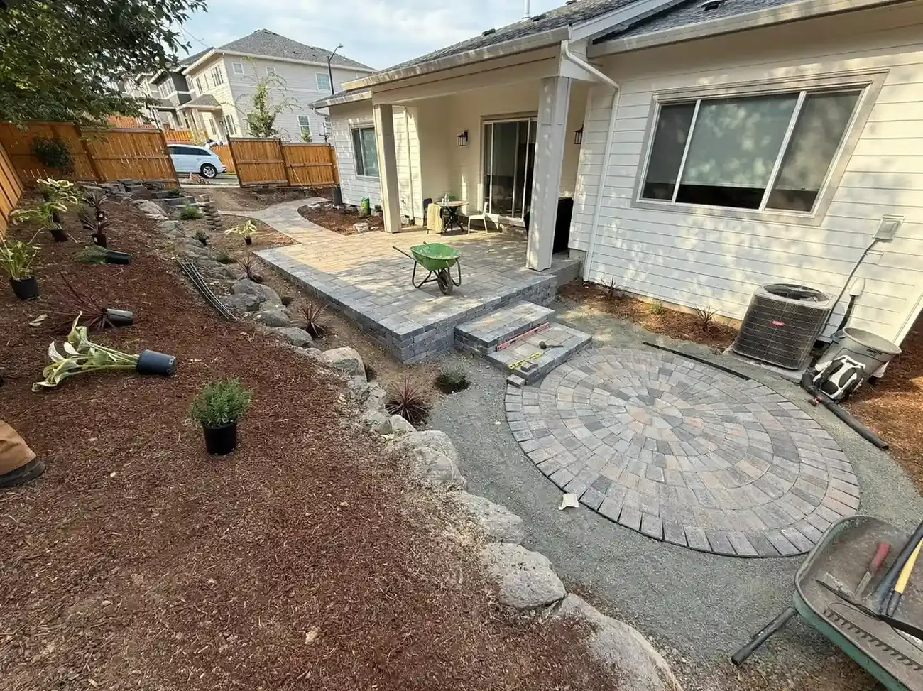 HD Landscape backyard circular paver installation with raised step platform and boulder landscape beds in Hillsboro