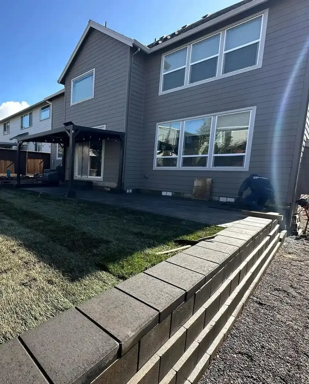 Block retaining wall installation in progress at residential backyard with pergola and lawn by HD Landscape in Tualatin