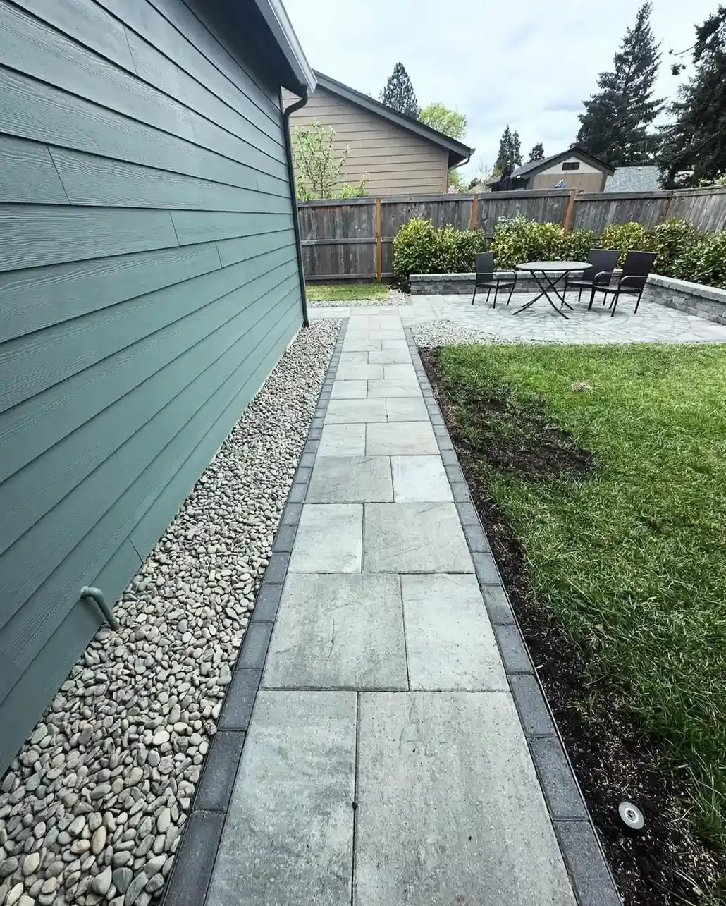 Paver walkway with river rock border leading to backyard patio seating area by HD Landscape in Hillsboro