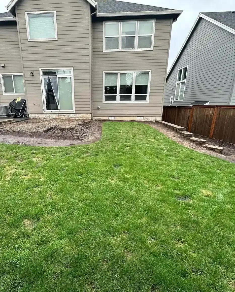 Residential backyard lawn with patio excavation in progress and stone steps along fence by HD Landscape in Salem