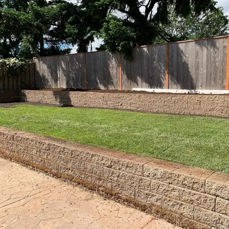 Terraced block retaining walls with fresh sod and flagstone patio in a fenced backyard by HD Landscape in Tualatin
