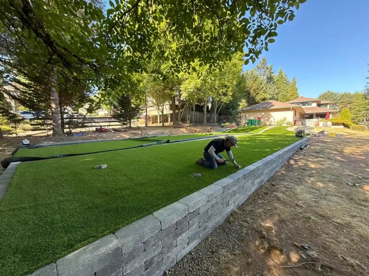 HD Landscape crew member installing artificial turf above a block retaining wall during backyard renovation in Sherwood