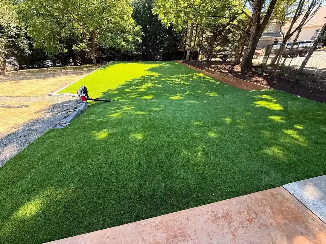 Freshly installed artificial turf lawn with wood border edging and concrete patio edge by HD Landscape in Clackamas