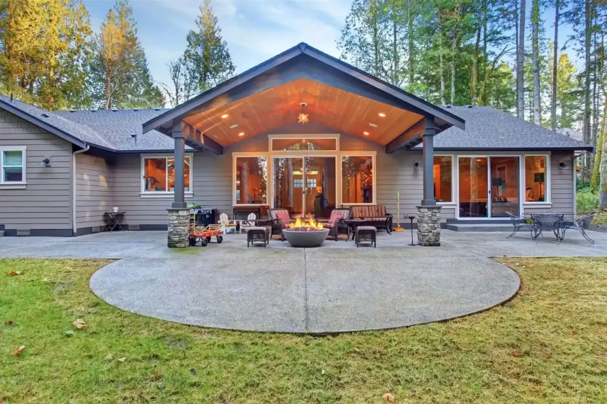 Circular concrete patio with fire pit seating area and covered outdoor room with stone columns by HD Landscape in Tualatin