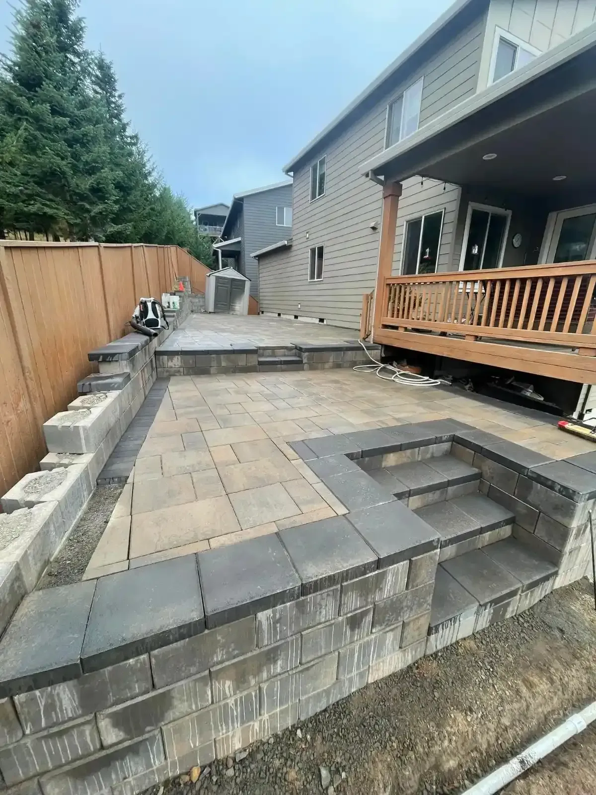 Multi-level paver patio with block retaining walls and steps under construction next to wood deck by HD Landscape in Wilsonville