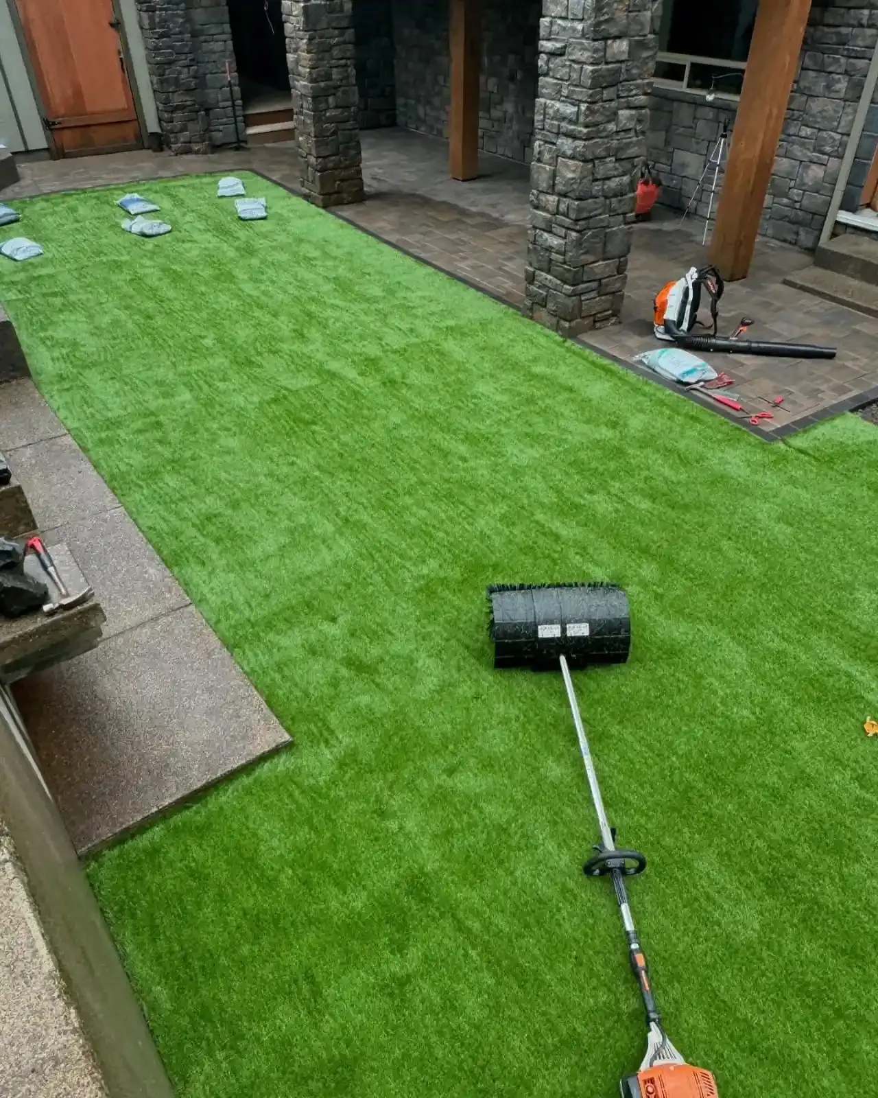 Artificial turf installation in a stone column courtyard with paver surround by HD Landscape in Lake Oswego