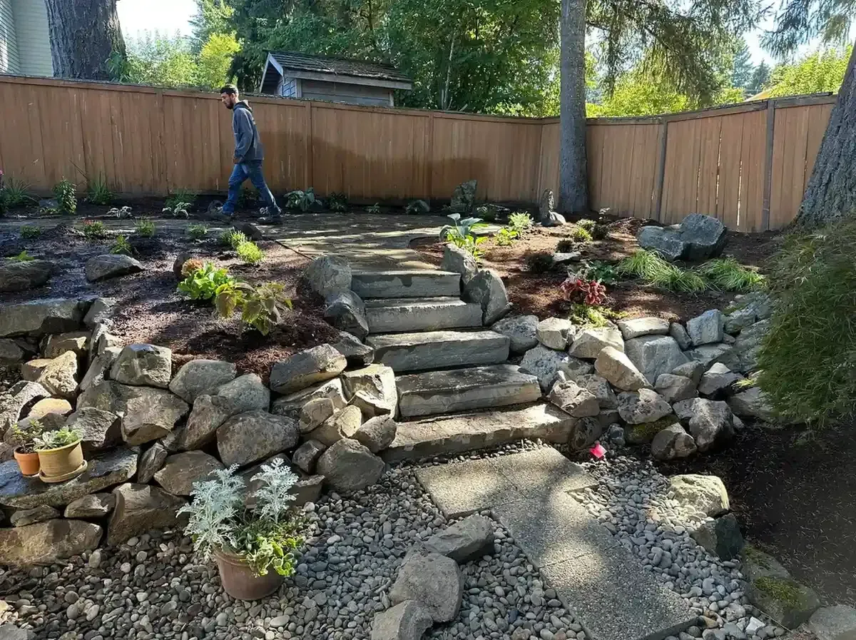 Natural boulder retaining wall with flagstone steps, river rock path, and new garden plantings by HD Landscape in Lake Oswego