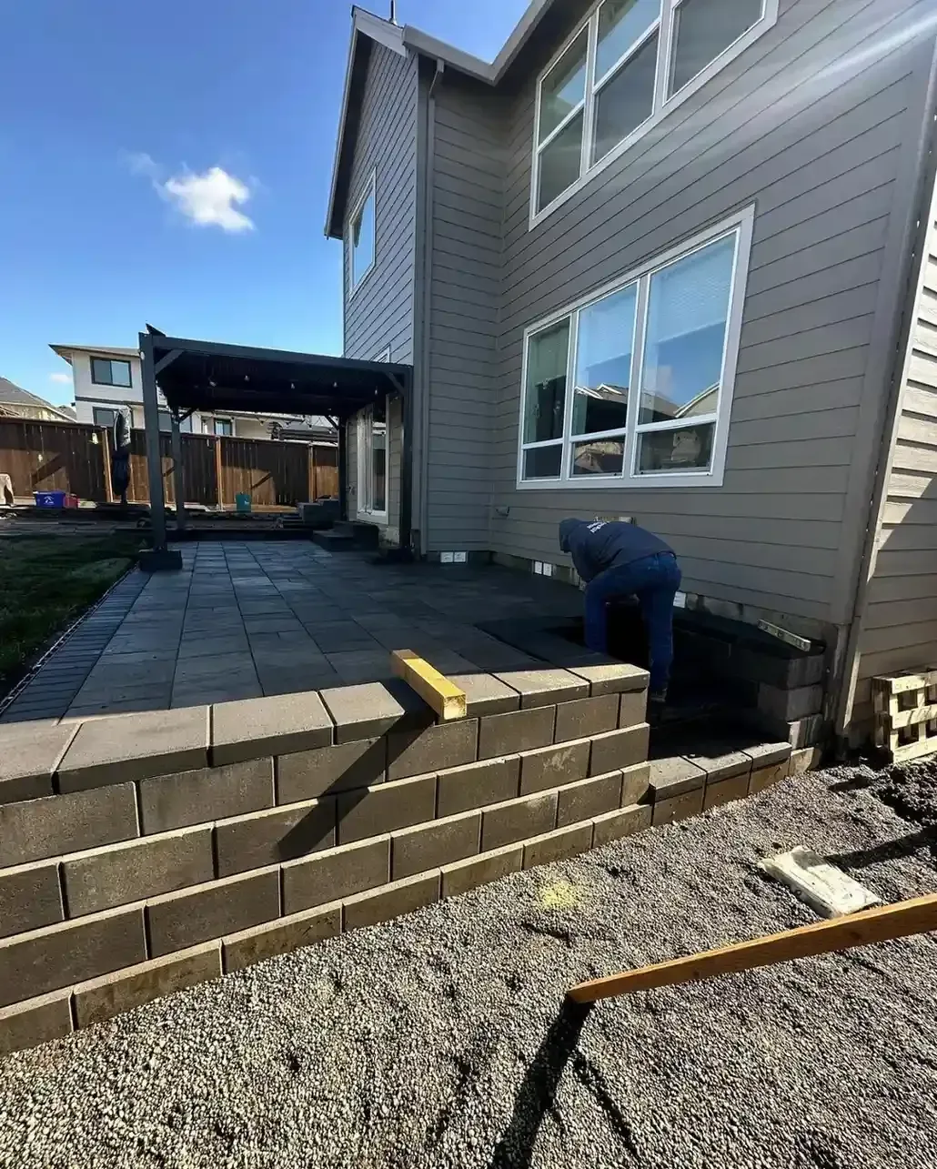 HD Landscape crew building a block seating wall beside a large format dark paver patio with pergola in Wilsonville