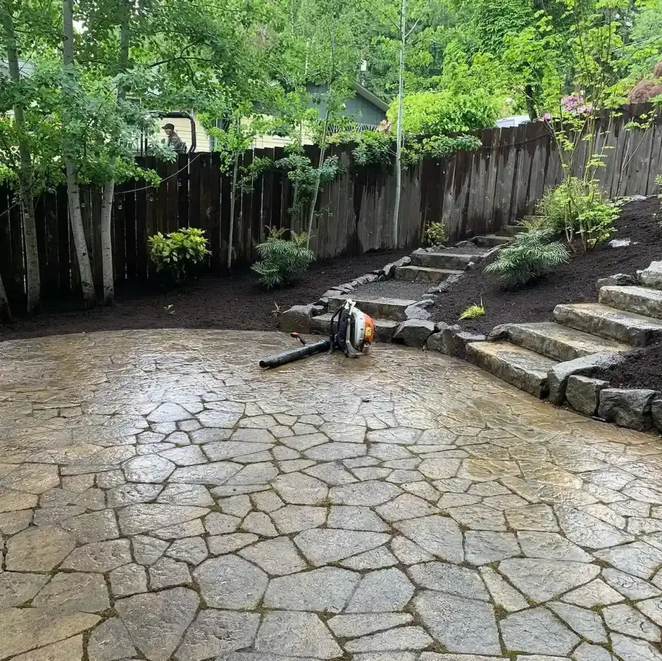 Wet natural flagstone patio with boulder retaining steps and fresh mulch planting beds by HD Landscape in Portland