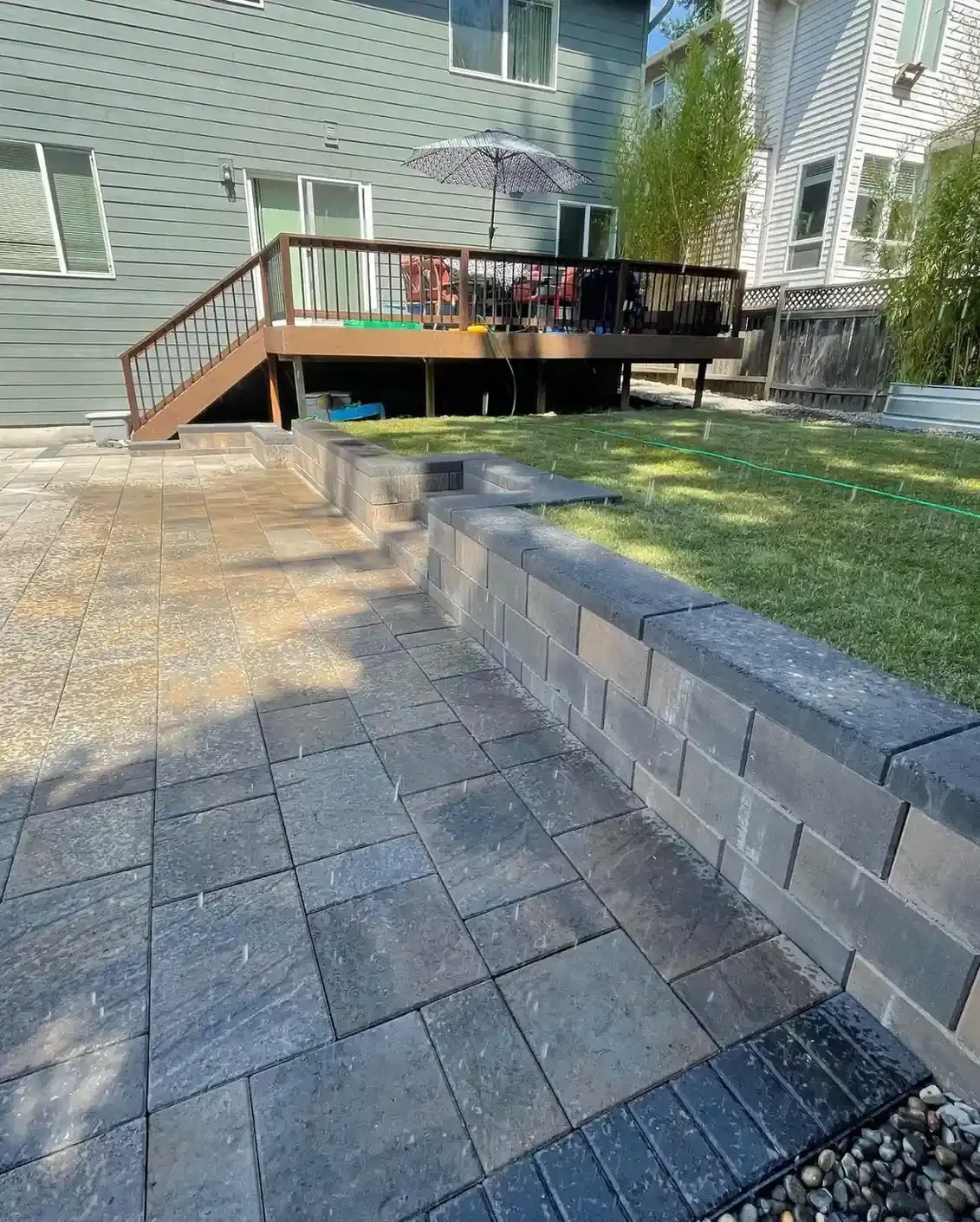 Large format charcoal paver patio with block seating wall, paver steps, and river rock edging by HD Landscape in Portland