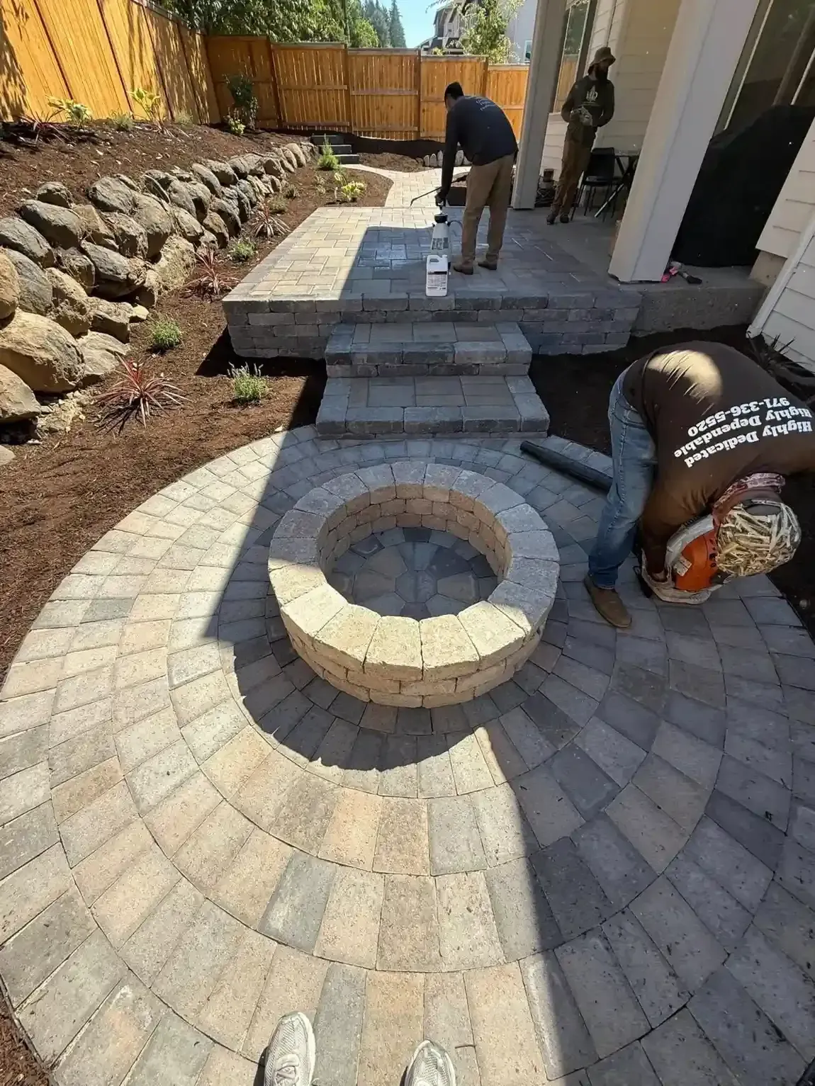 HD Landscape crew installing a circular paver patio with built-in stone fire pit ring and paver steps in Beaverton