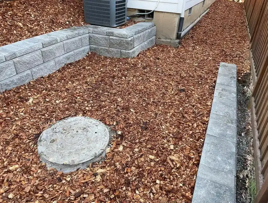 Block retaining wall enclosure around AC unit with cedar chip mulch and concrete curbing by HD Landscape in Beaverton