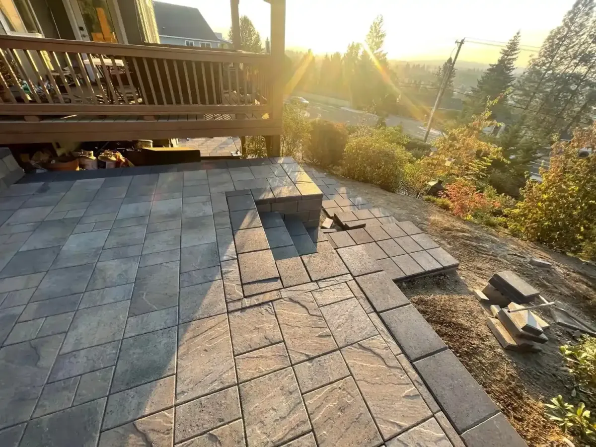 Paver patio with built-in block seating wall under construction at sunset on a hillside property by HD Landscape in West Linn