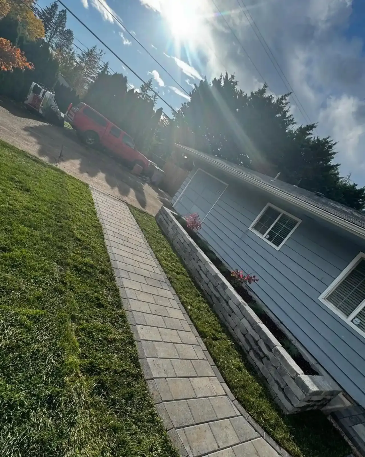 Paver walkway alongside a block retaining wall with flowering planter and manicured lawn by HD Landscape in Clackamas