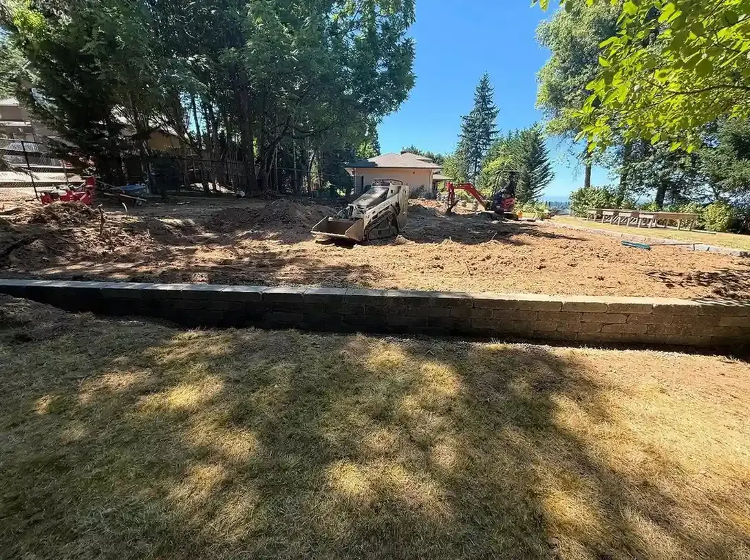 HD Landscape skid steer and mini excavator grading a hillside lot above a completed block retaining wall in West Linn