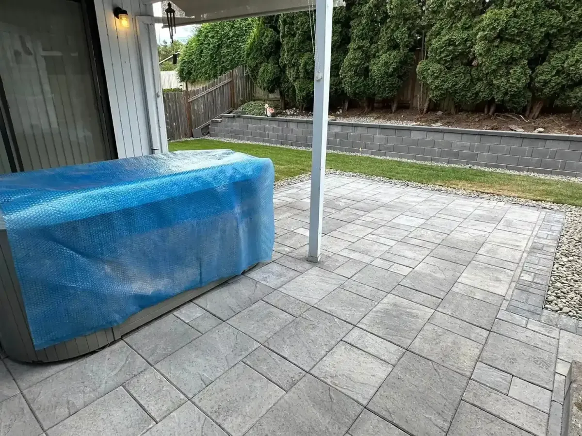 Paver patio with hot tub pad, block retaining wall, river rock border, and lawn by HD Landscape in Tualatin
