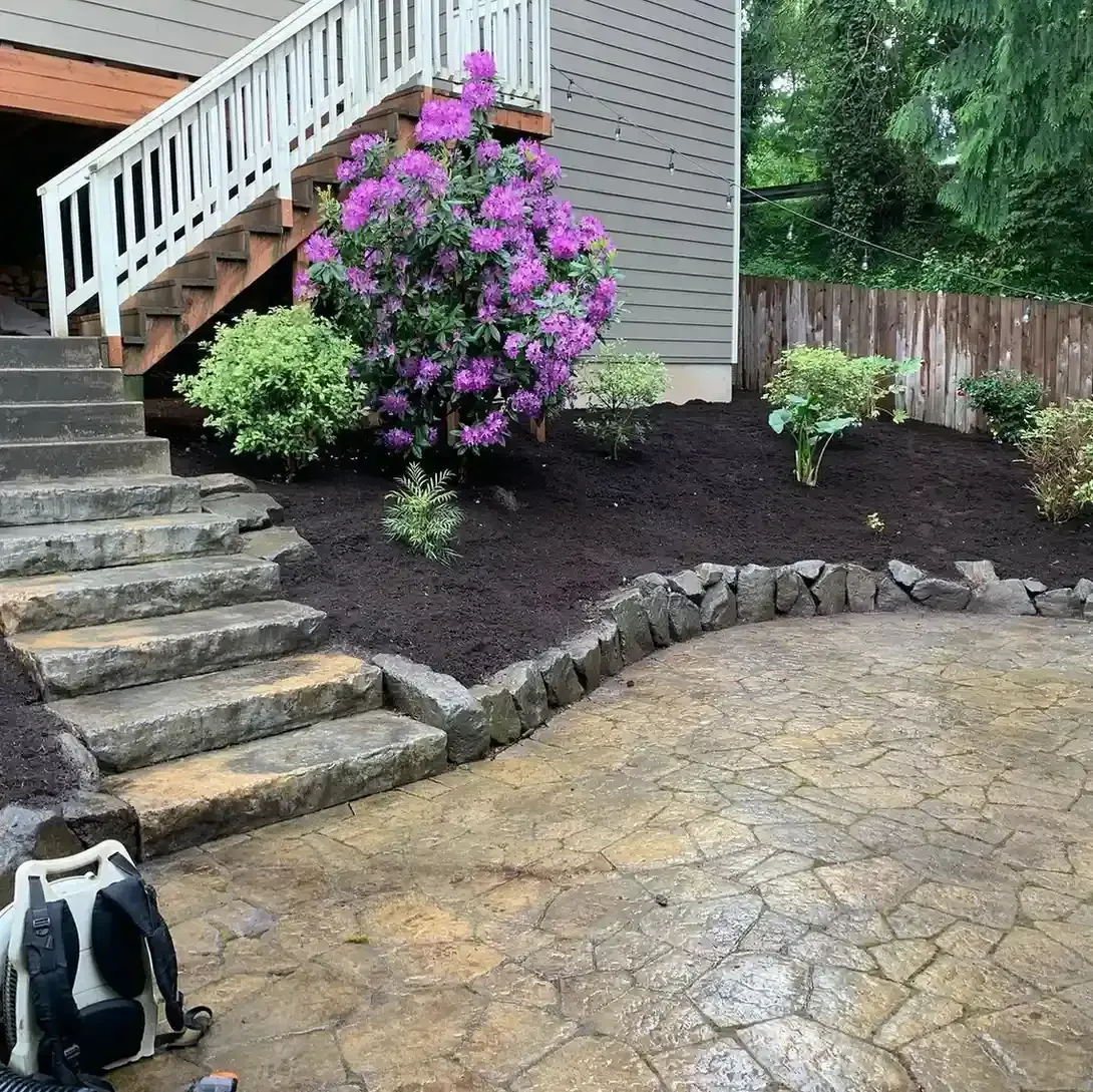 Flagstone patio with natural stone steps, rock border, and blooming rhododendron installed by HD Landscape in Portland