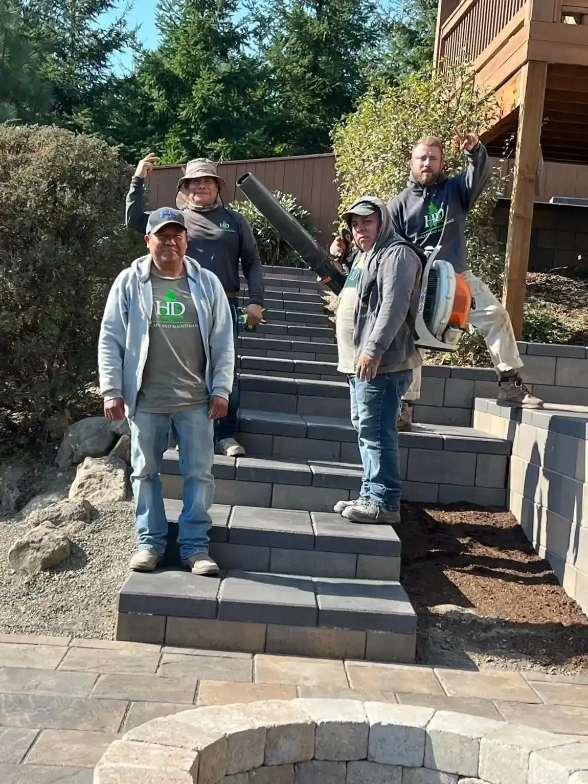 HD Landscape and Maintenance four-man crew posing on completed paver steps and fire pit patio in West Linn