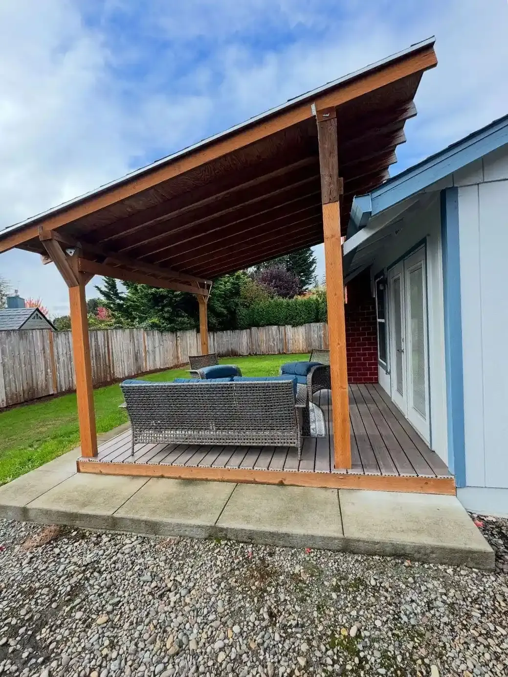 Covered lean-to pergola with composite deck, outdoor seating, gravel border, and manicured lawn by HD Landscape in Salem