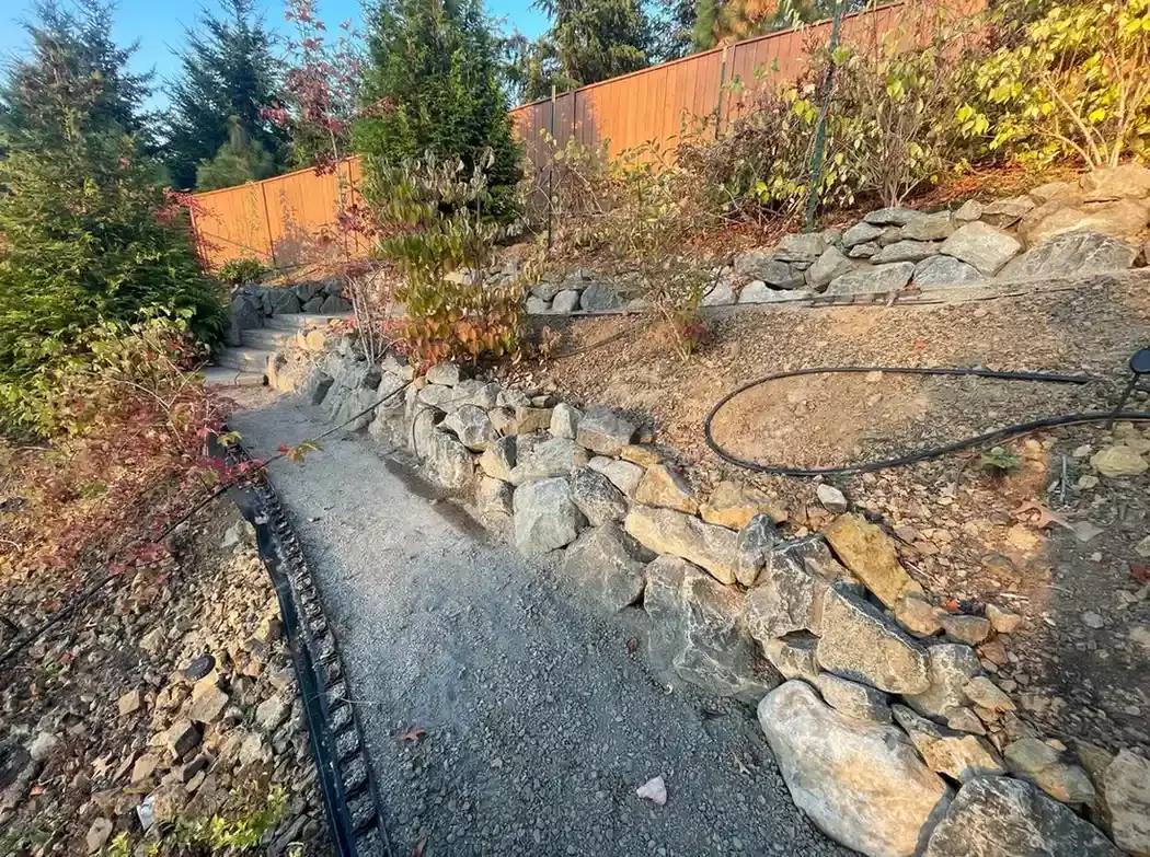 Dry-stacked boulder retaining wall with gravel pathway and drip irrigation on a hillside lot by HD Landscape in West Linn