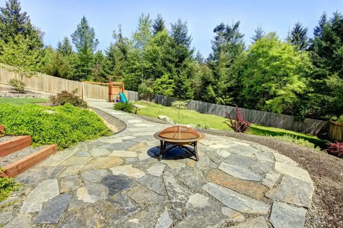 Flagstone patio with fire pit bowl, curved garden path, and wooded backyard in West Linn
